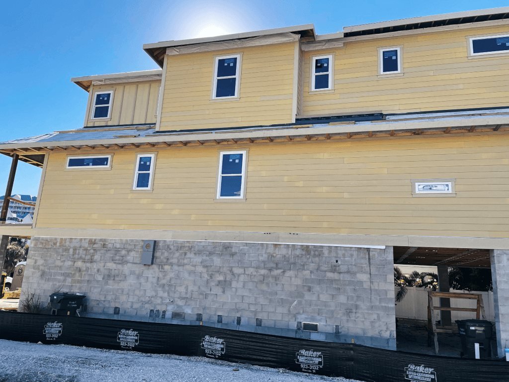 Elevated coastal home under construction by Acosta Builders — impact windows, lap siding, and structural framing above a block base