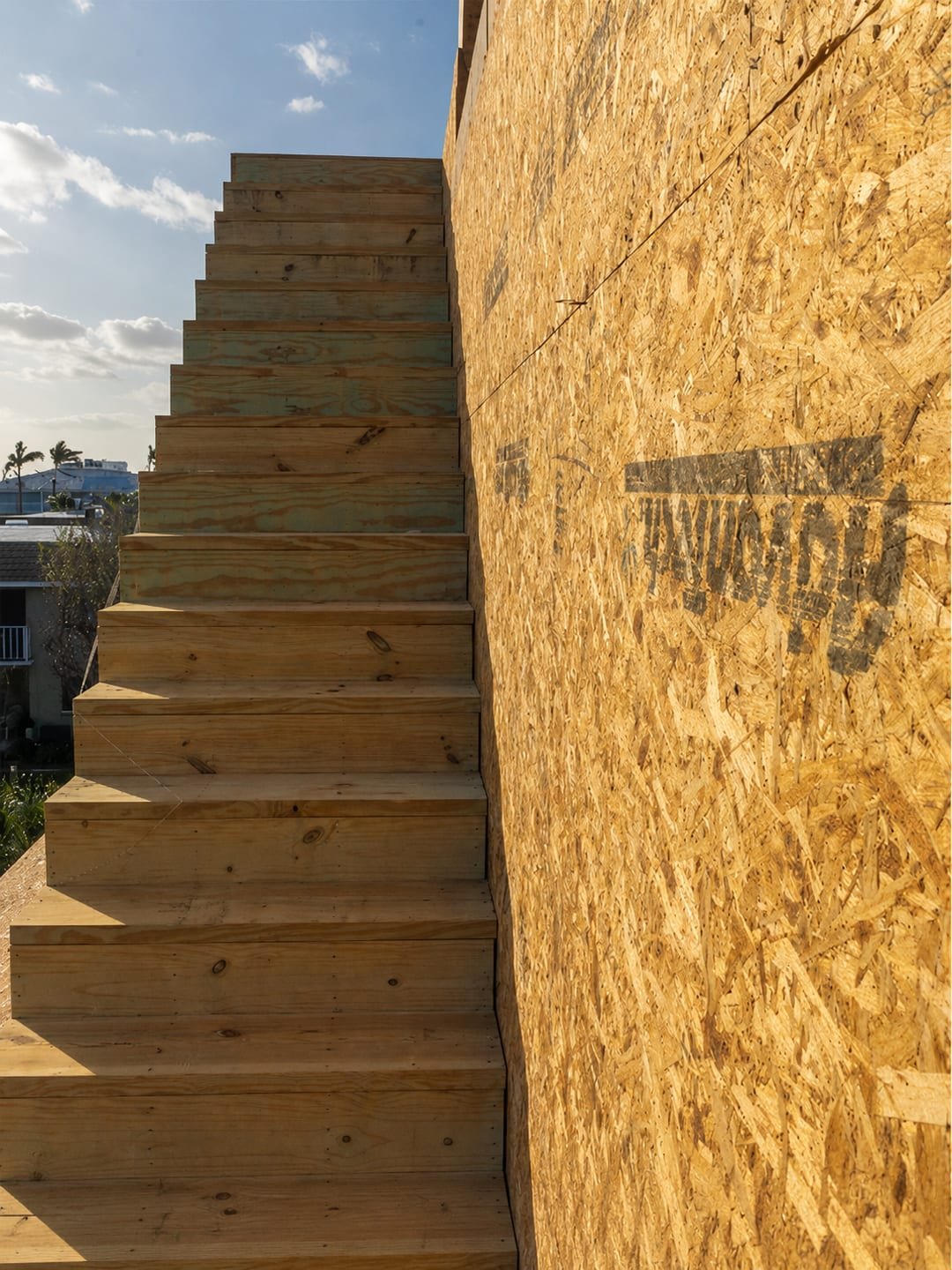 Framed exterior stair by Acosta Builders climbing an OSB-sheathed wall to a second-story addition